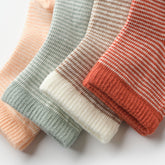 Close-up of striped baby socks in peach, sage, cream, and terracotta tones